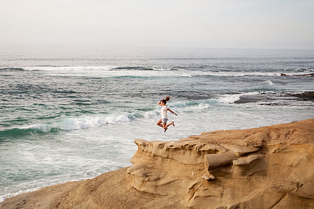woman jumping on hill near ocean during daytime thumbnail