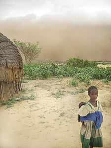 girl in yellow and green dress carrying baby on her back beside hut during daytime thumbnail