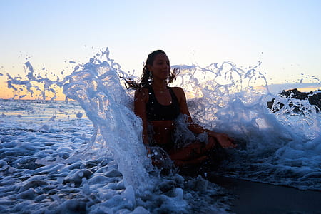 woman sitting on beach smiling while her back strike by sea waves thumbnail