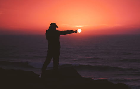 silhouette photography of person standing in front of body of water during golden hour thumbnail