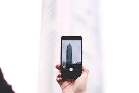 person holding black smartphone taking picture white concrete tower building thumbnail