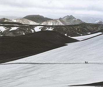 two people walking in middle of snow near mountains thumbnail