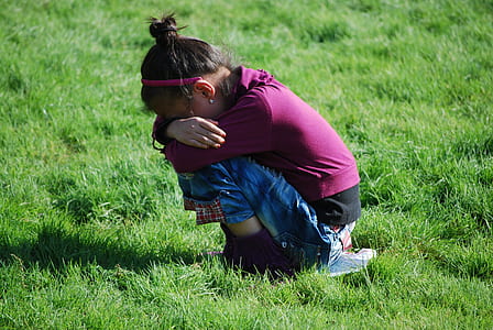 girl wearing maroon long-sleeved top and blue jeans sitting on green grasses during daytime thumbnail