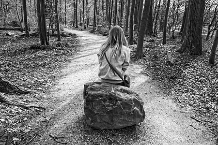 grayscale photography of woman sitting on rock in middle of dirt road thumbnail
