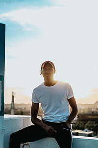 man sitting on rooftop edge wearing white shirt and red fitted cap thumbnail