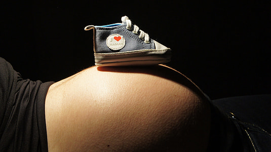 unpaired baby's blue high-top crib shoe on woman's belly thumbnail
