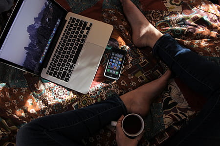 person sitting beside MacBook Pro and space gray iPhone 5 while holding mug thumbnail