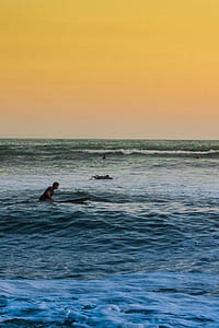 Man Swimming on Sea Under Yellow Sky thumbnail