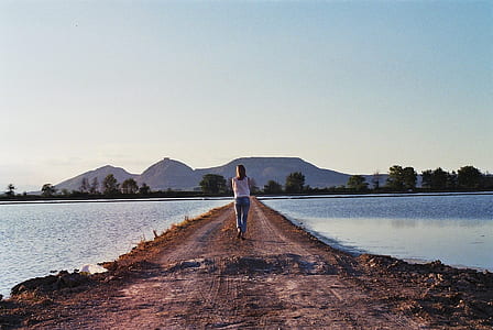 woman wearing blue jeans and white top near body of water at daytime thumbnail