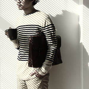 Standing Brunet Person Waring Eyeglasses and White Black Stripe Sweater Holding Mug and Briefcase thumbnail