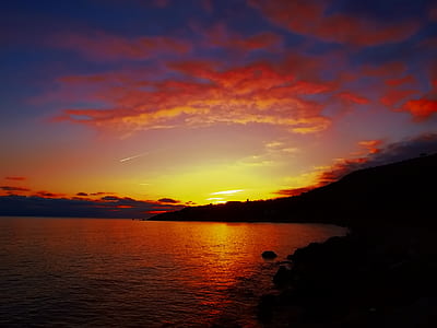 silhouette photo of mountains near open sea under cloudy sky during golden hour thumbnail
