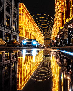 reflection of cars and people walking on sidewalk near buildings with lighted string lights during night time thumbnail