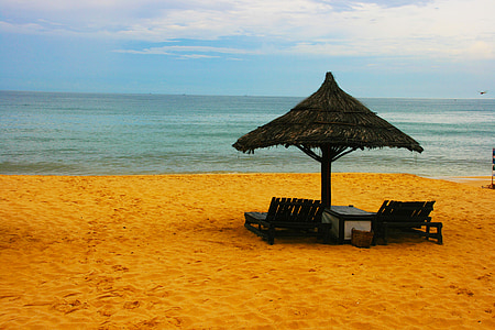 two lounge chairs under black wicker umbrella facing sea at daytime thumbnail