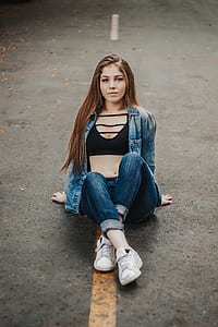 woman wearing blue acid-washed denim jacket and black crop top sitting down on the middle of concrete road thumbnail
