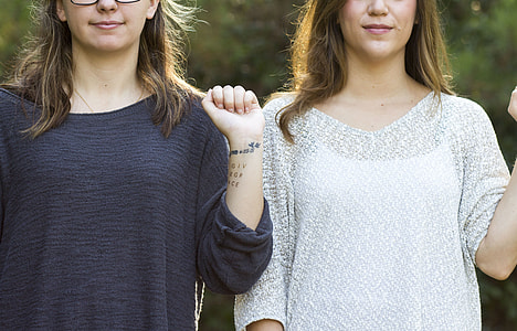 selective focus photography of two women wearing white and black shirts showing left wrist tattoos thumbnail