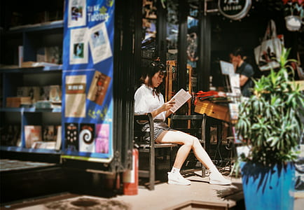 woman sitting on wooden bench while reading book during daytime thumbnail