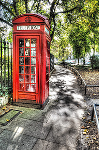 red telephone booth beside black metal fence under tree at daytime thumbnail