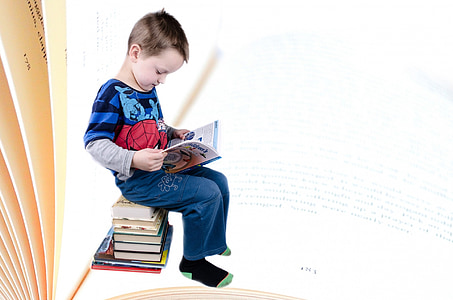 toddler in Spiderman printed shirt sitting down on pile of books reading book thumbnail