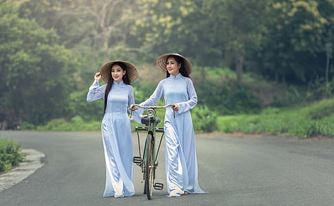 two woman with hat walking in street with bicycle thumbnail