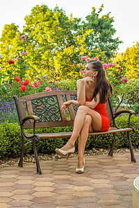 woman wears red mini dress sits on brown bench thumbnail