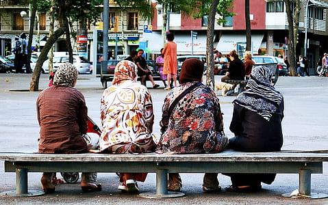 four women sitting on bench on side of street thumbnail