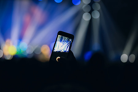 A person uses the camera in the crowd on his mobile smartphone at a music concert party event thumbnail