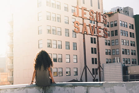 , woman sitting near building and Jesus saves signage thumbnail