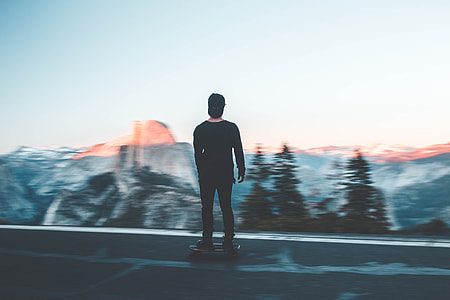 man riding on skateboard near pine trees and mountain thumbnail