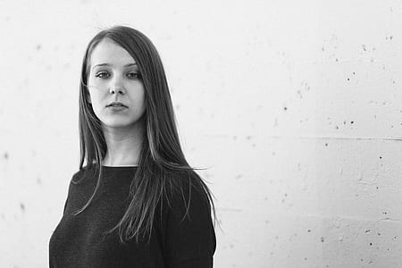 grayscale photography of woman standing in front of white concrete wall wearing black top thumbnail