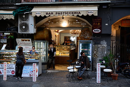 man sitting near woman standing near Bar Pasticceria signage thumbnail