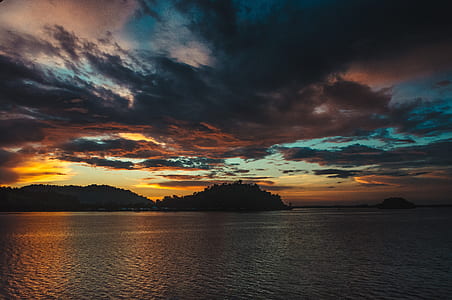 silhouette photo of rock formation on calm body of water thumbnail