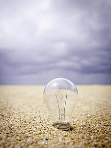 clear glass light bulb surrounded by brown sand during daytime thumbnail