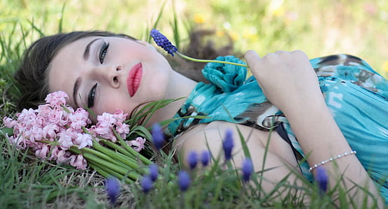 woman lying on grass field holding grape hyacinth flowers thumbnail