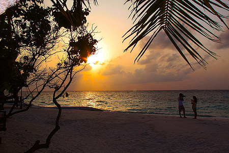 two people standing on the beach near body of water during sunset thumbnail