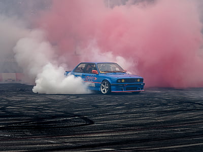 blue sedan drifting and burning off wheels on asphalt road thumbnail