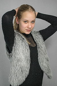 woman in gray fur vest and black long-sleeved shirt holding her head thumbnail