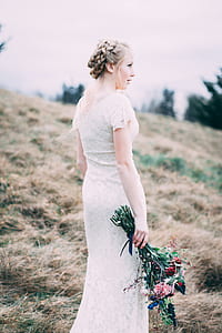 bride holding pink and red rose flowers bouquet on hill near trees under white skies daytime thumbnail