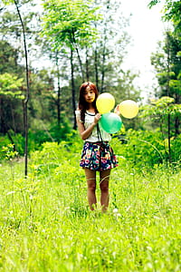 Woman Standing on Grass Field While Holding Three Balloons thumbnail