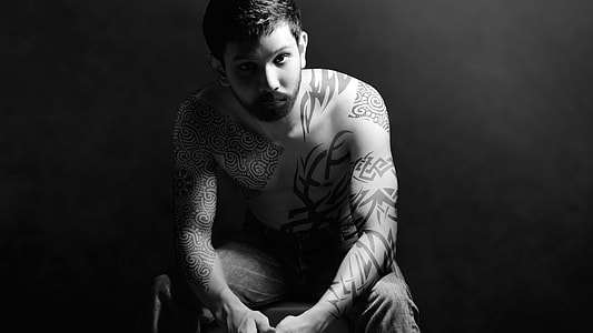 man with body tattoo sits on chair thumbnail