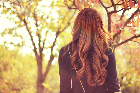 shallow focus photography of brown haired woman in black long sleeve top standing facing back near green leaf trees thumbnail