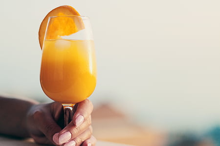person holding orange juice on goblet glass thumbnail