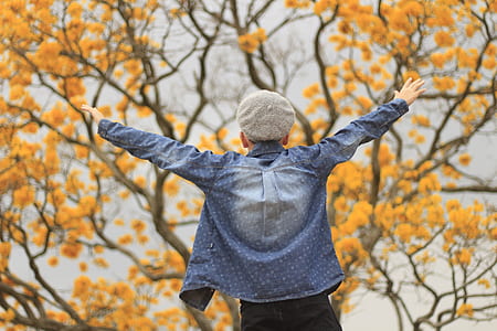 shallow focus photography of man in blue dress shirt standing in front of yellow leaves tree thumbnail