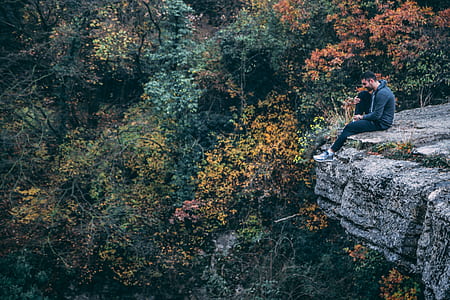Man In Hoodie Sitting On Rock Cliff thumbnail