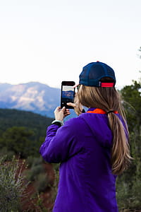 Woman Holding Smartphone While Taking Picture of Mountain thumbnail