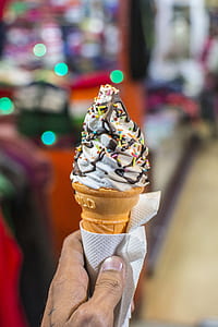 person holding wafer cone with soft-served ice cream topped with sprinkles and chocolate thumbnail