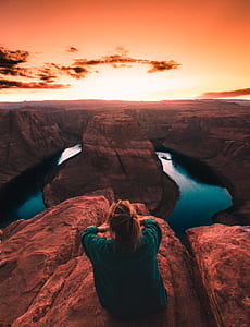 woman sitting on mountain cliff facing horseshoe bend during golden hour thumbnail