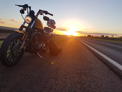 black cruiser motorcycle parked beside paved road during sunset thumbnail