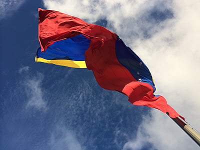 blue, red, and yellow waving flag under cloudy blue sky thumbnail