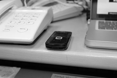 selective photo of candybar phone between telephone and laptop on table thumbnail