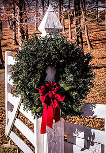 green and red wreath hang on white wooden fence during daytime thumbnail